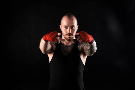 Fighter show into the camera. Man with muscular body and tattoo in black t-shirt on dark background. Showing concept.の写真素材