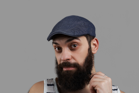 Close up high detailed portrait of caucasian bearded man isolated on grey background and look to the camera. Male keep beard by hand and think about bottle of beer or new sea trip. Time to dream.の写真素材