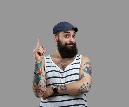 Have an idea. Bearded brutal man in singlet with tattooed body point finger up. Surprised emotion on face. Take atantion for a sale.の写真素材