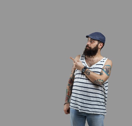 Beard man with tattooed hands point and look to the right. Copy space for advertising goods or promotion text. Guy with big beer stomach. Unhealthy food liker.の写真素材