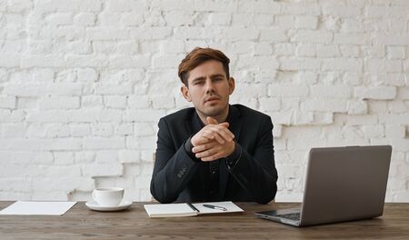 Interested stylish designer listen client and rub hands. Man in office sit at the table with...