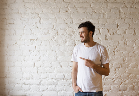 Handsome hipster point to the right side and look away on white brick background. Man have good mind and attractive smile. Free space for advertising text and promotion product.の写真素材