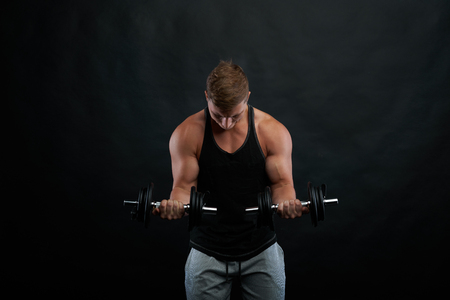 Hard trainig on biceps with dumbbels. Train strong body. Athletic exercises on black background. Front view on working gym trainer.の写真素材