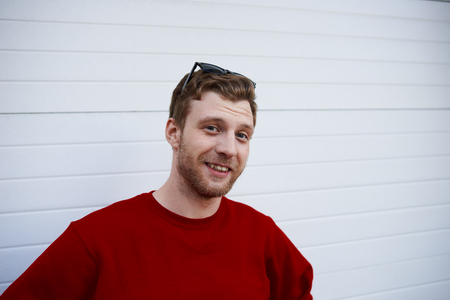 People and modern lifestyle concept. Outdoor portrait of attractive student with beard wearing sunglasses on his head looking and smiling at camera, feeling relaxed after lectures at universityの写真素材