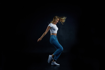 Full lenght studio shot of blonde European girl wearing crop top and blue stretch jeans stretching, doing aerobics or dancing. People, sports, fitness, dance, energy, flexibility and active lifestyleの写真素材