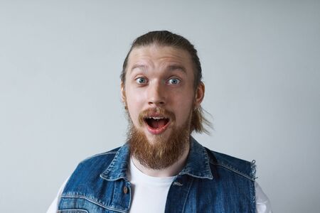 Headshot of excited astonished stylish young European man with thick beard and hair gathered in knot raising eyebrows and opening mouth widely in surprise and astonishment. Human reaction and attitudeの写真素材