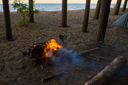 Outdoor summer shot of campsite with fireplace, camping tent in wild nature. Somebody set camp among trees in forest on beach by river or sea. Hiking, trekking, adventure and traveling conceptの写真素材