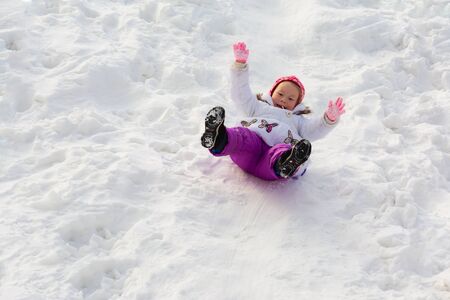 The little girl slides sitting on an ice slopeの写真素材