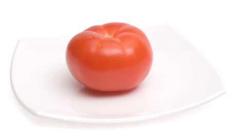 Red ripe tomato lying on a white square ceramic plateの写真素材