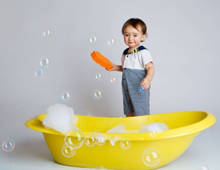 Baby with sponge standing beside yellow bathtub