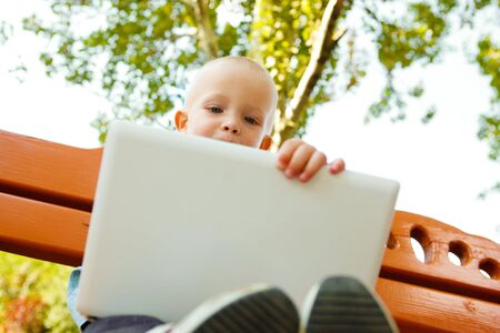 Cute boy sitting on the bench with  laptopの写真素材