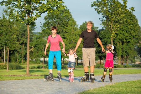 Parents and two daughters skating in a summer parkの写真素材