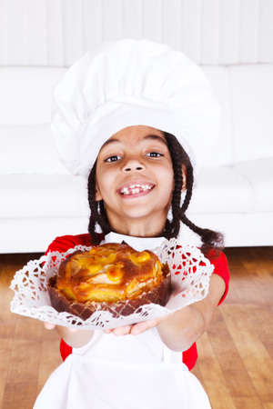 Smiling african american girl in apron and hat giving an apple pieの写真素材