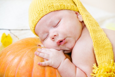 Portrait of a baby in yellow hat using pumpkin as a pillowの写真素材