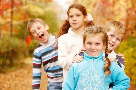 Kids stand one behind another in autumnal parkの写真素材