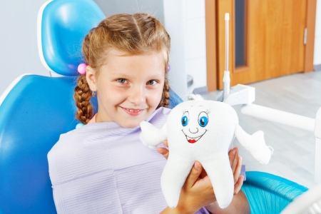 Cheerful child in dentist seat holding a toy toothの写真素材