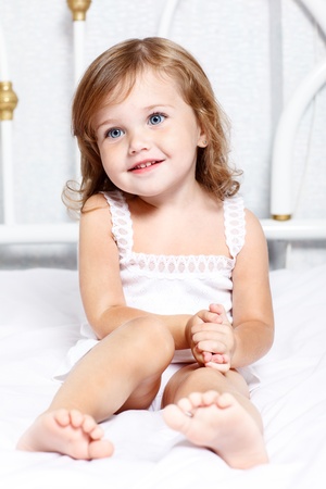 Sweet thoughtful little girl sits in bedの写真素材