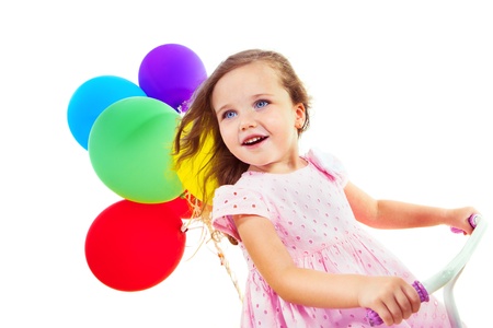 Portrait of a cheerful little girl on a bike, with colorful balloons behindの写真素材