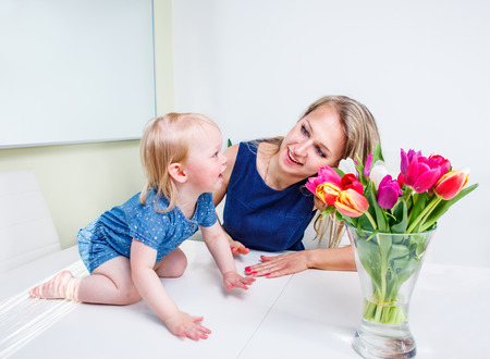 Laughing toddler girl on the table plays with momの写真素材