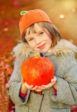 Autumn girl wearing orange hat and holding pumpkin in hands. Warm sunlight background.の写真素材