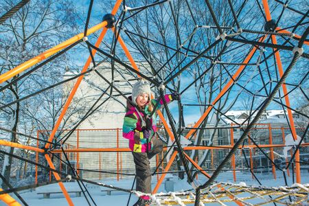 Kid in winter clothing climbing kids net at the playgroundの写真素材