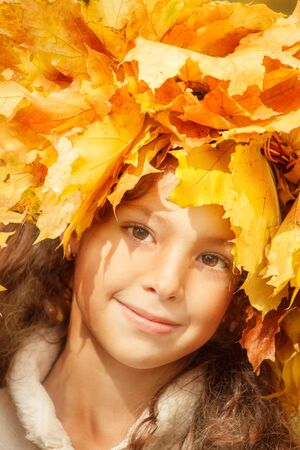 Closeup portrait of a school girl with yellow autumn leaves on her headの写真素材
