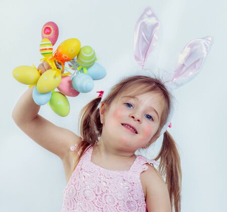 Smiling preschool kid with Easter bunny ears on holding a bunch of colorful eggsの写真素材