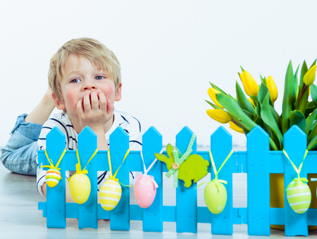 Llittle boy lying behind an artificial blue fence with Easter decorationの写真素材