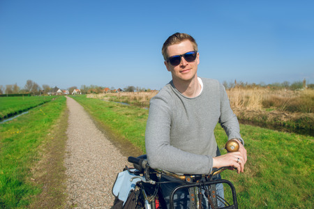 Portrait of a man standing with a bicycle  in a countryside in early springの写真素材