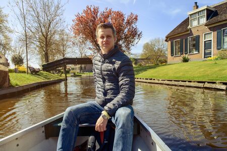 Tourist in a rented boat is taking a tour through Giethoorn village in the Netherlandsの写真素材