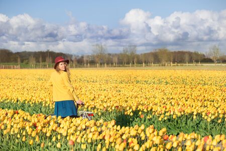 Smiling woman standing with her bike in a yellow and red tulips field at sunset.の写真素材