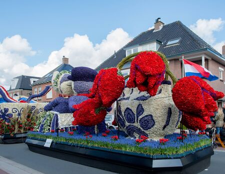 HILLEGOM, THE NETHERLANDS - APRIL 23, 2016: Moving platform with a huge frame made in a form of a traditional Dutch kissing couple and vase with tulips.  Every carcass is decorated with spring flowers. Taking part in the  traditional flowers parade "Bloemのeditorial素材