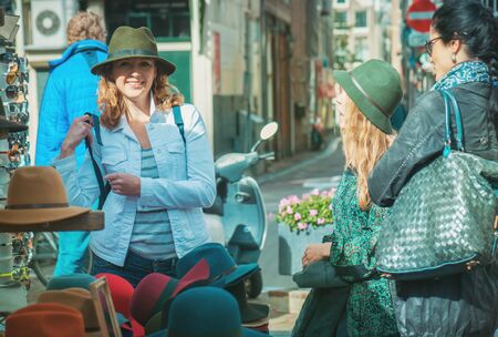 Female friends trying on hats at the street marketの写真素材