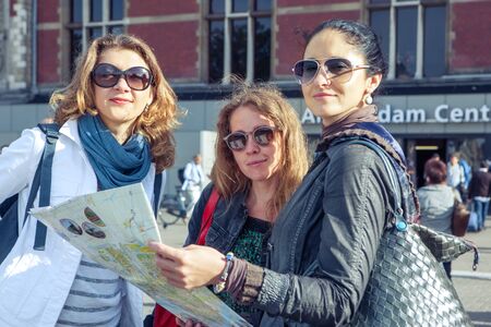 Three female tourists holding a map at the main railway station in Amsterdam, Dutch capitalの写真素材