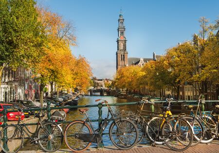Bicycles standing near scenic Amsterdam canal in autumn. Famous Westerkerk is in the backgroundの写真素材