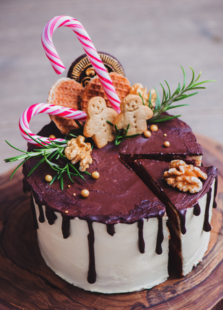 Homemade Christmas cake decorated with cookies, candy canes, nuts and rosemary on a rustic wood standの写真素材