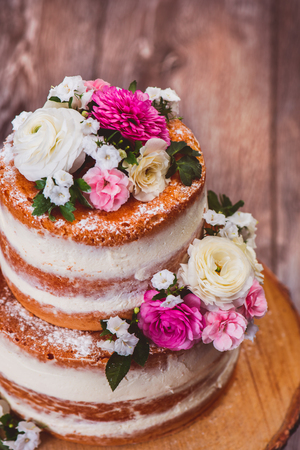 Closup shot of a two layered homemade naked cake  decorated with flowers on wooden cut standの写真素材