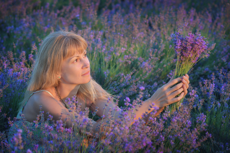 Young beautiful woman with long blond hair on lavender field. Blonde with long hair in dress on background of lilac field at sunsetの写真素材