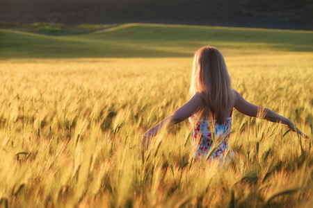 Young beautiful woman with long blond hair on wheat field. Blonde with long hair in dress on background of wheat field at sunsetの写真素材