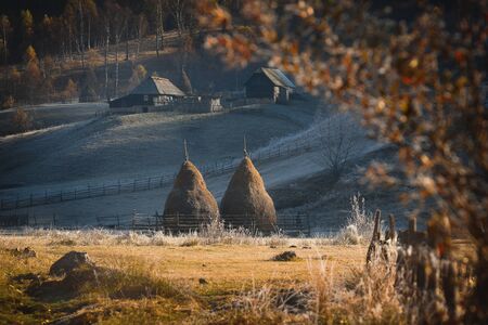 Frosty autumn morning in the village of shepherds Fundatura Ponorolui, Transilvania, Romania. Rural landscape with wooden houses and haystacksの写真素材