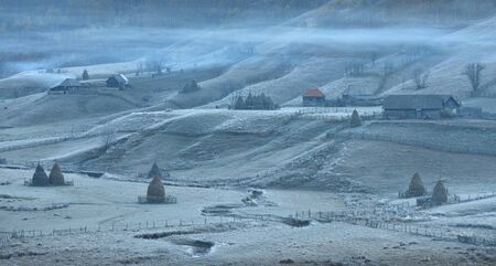 Frosty autumn morning in the village of shepherds Fundatura Ponorolui, Transilvania, Romania. Rural landscape with wooden houses and haystacksの写真素材