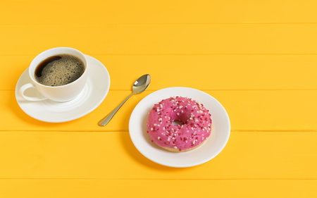 Coffee and Pink Donut with Spoon on Yellow Wooden Backgroundの写真素材