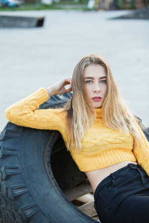 Portrait. A beautiful sexy girl, blonde, a young woman who looks like Jennifer Aniston lies in the ruins, a large rubber wheel from the tractor. Light against the sun. Red lips.の写真素材