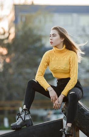 Portrait beautiful sexy girl blonde a young woman who looks like Jennifer Aniston sits in the ruins a big large rubber wheel from the tractor Light against the sun Looks in the direction of the wind.の写真素材