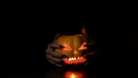 Young woman fooling around with a pumpkin. Halloween holiday. Gives creepy horns. Isolated black background.の写真素材