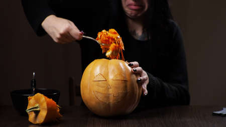 Young brunette woman carves a pumpkin for Halloween. Preparation for the holiday.の写真素材