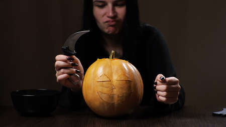 Young brunette woman carves a pumpkin for Halloween. Preparation for the holiday.の写真素材