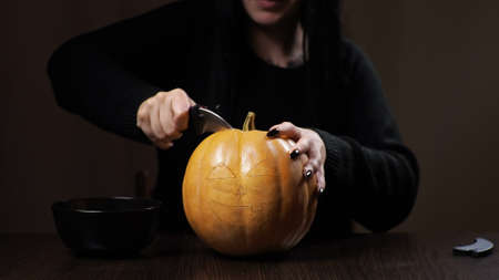 Young brunette woman carves a pumpkin for Halloween. Preparation for the holiday.の写真素材