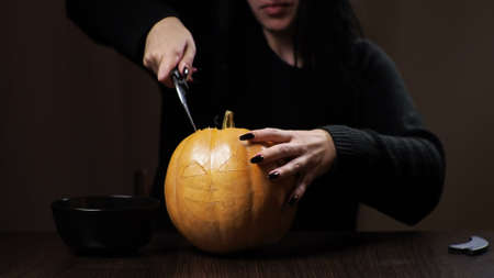 Young brunette woman carves a pumpkin for Halloween. Preparation for the holiday.の写真素材