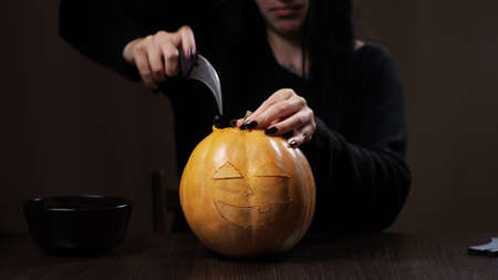Young brunette woman carves a pumpkin for Halloween. Preparation for the holiday.の写真素材